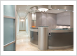 Modern dental clinic reception area with a curved front desk, built-in cabinets, glass shelves, and a bright hallway leading to treatment rooms.