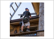A technician installs a gutter guard while standing on a ladder at a home’s roofline.