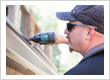 A worker secures a metal gutter using a power drill along a home’s roofline.