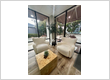 A cozy and inviting waiting area with two cream-colored boucle chairs, a wooden cube coffee table adorned with a glass terrarium centerpiece, surrounded by large windows offer